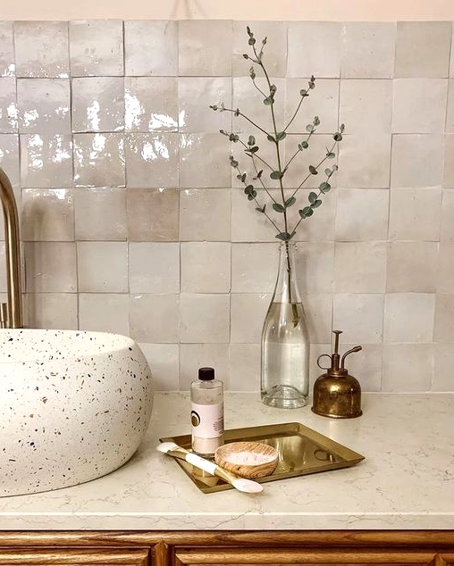 a gorgeous bathroom with a vintage feel, with neutral zellige tiles, a terrazzo sink, a white stone countertop and brass fixtures
