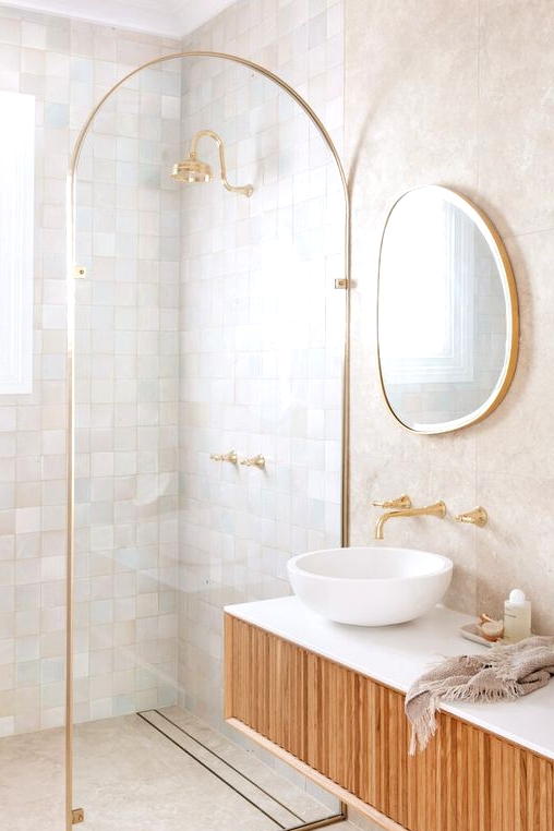 a refined bathroom clad with neutral and pastel zellige tiles in the shower, with a curved space divider and a floating wooden vanity