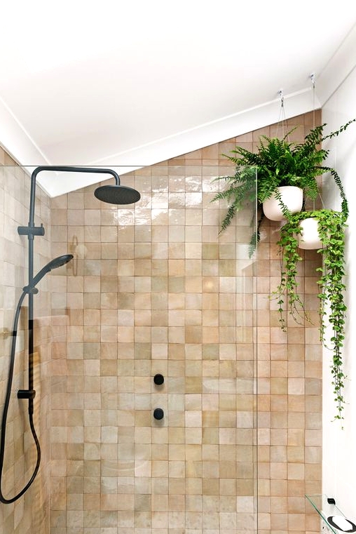 an attic shower space clad with blush and tan zellige tiles, with suspended potted plants and black fixtures for a modern feel