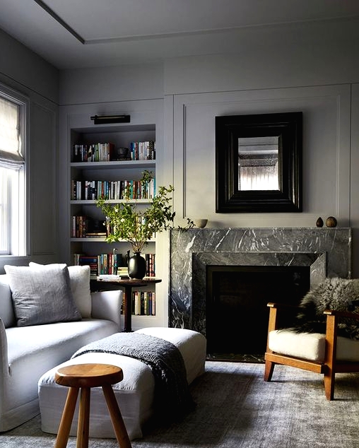 a neutral living room with dove grey walls and built-in shelves, a white sofa and a bench, a fireplace clad with black marble