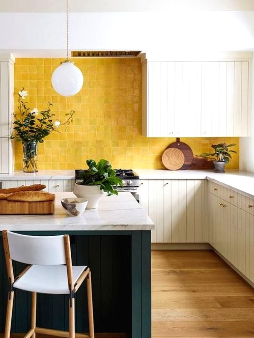 a chic vintage-inspired kitchen with white beadboard cabinets, white stone countertops, a sunny yellow tile backsplash and a hunter green kitchen island
