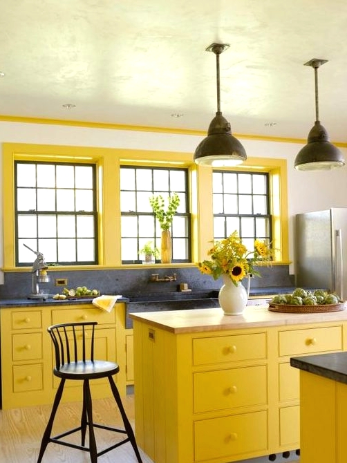 a bright farmhouse kitchen with bold yellow cabinets and window frames, grey stone countertops and a large sink