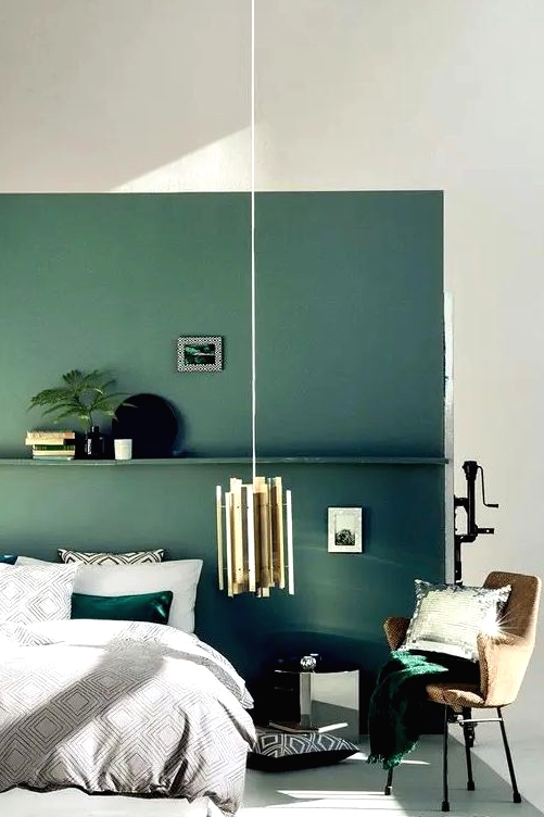 a muted green accent wall with a shelf and matching emerald bedding and a pillow