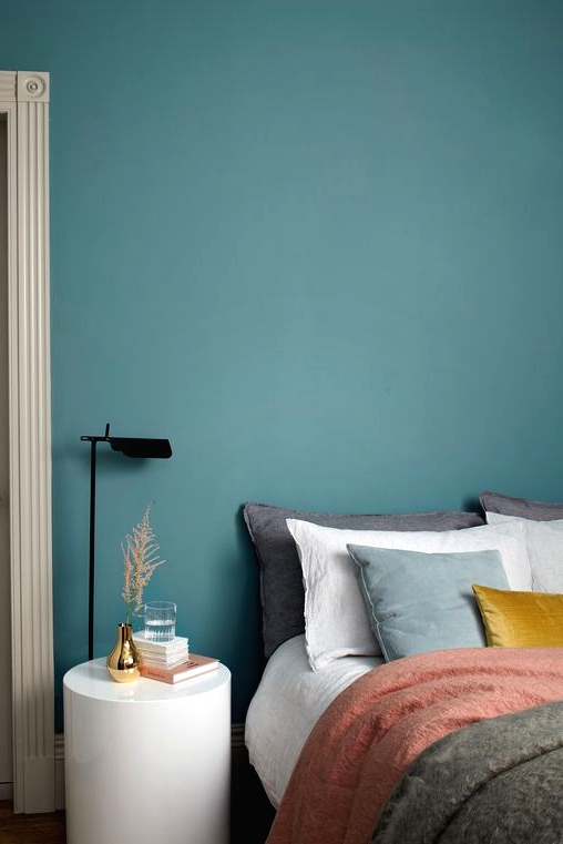 a soothing and chic stone blue bedroom with a bed with muted color bedding, a white round nightstand and a black lamp