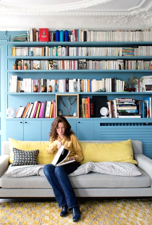 a living room and library done in stone blue - all the walls, shelves and storage units plus yellow accents in the space