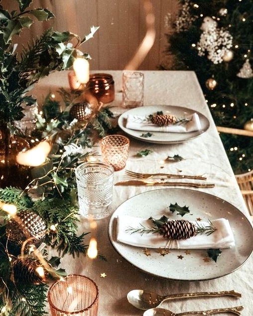 a bright christmas tablescape with an evergreen runner, lights, metallic ornaments, star print plates and copper candleholders