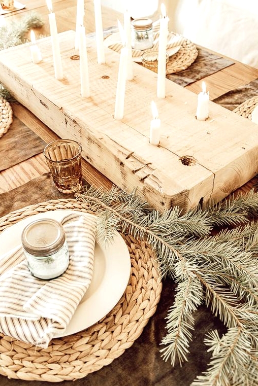 a hygge Christmas table with woven placemats, evergreens, striped napkins, a wooden board with tall and thin candles