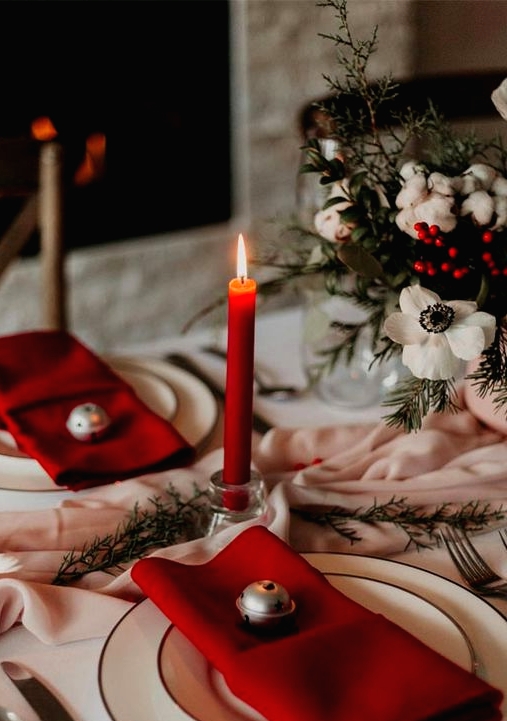 a lovely holiday tablescape with a blush runner, white blooms and red berries, red napkins and candles, simple gold-rimmed plates