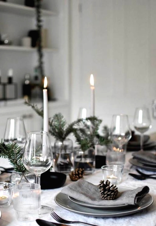 a Nordic Christmas table with tall and thin candles, evergreens, grey plates, neutral linens and simple glasses