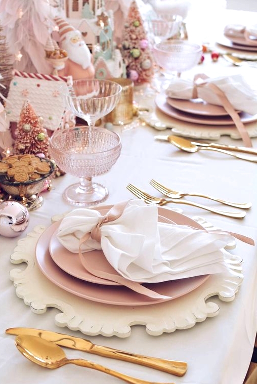 a pink Christmas tablescape with carved wooden placemats, pink plates, gold cutlery, pink Christmas trees, glasses and gingerbread houses