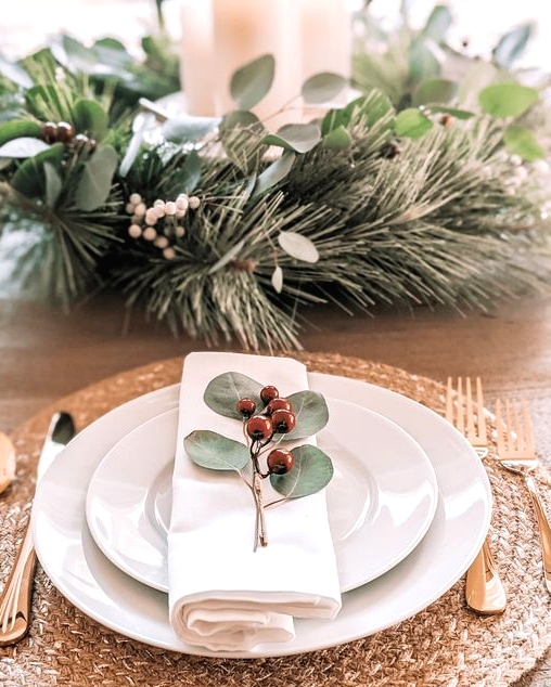 a pretty Christmas place setting with a woven placemat, white porcelain, evergreens and berries, gold cutlery is amazing