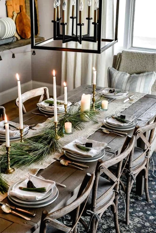 a pretty Christmas table with a white table runner and napkins, tall and thin candles, a greenery runner and grey porcelain is chic and simple