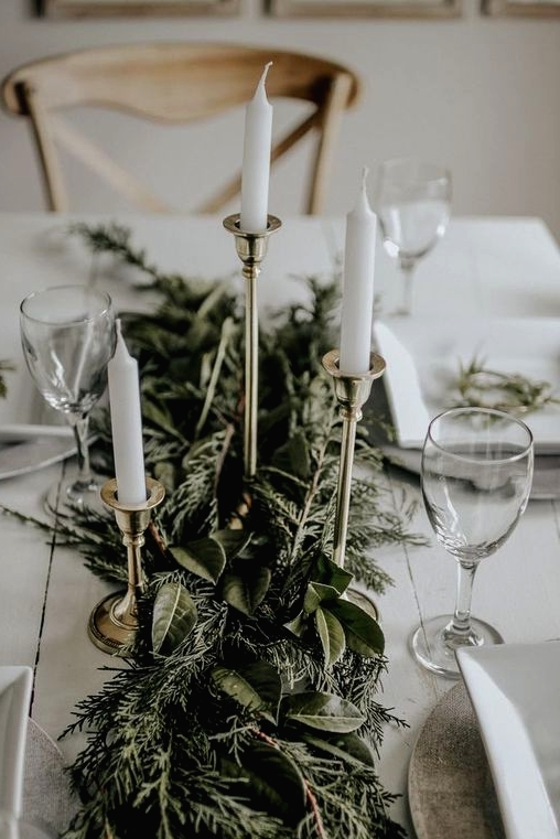 a sophisticated Christmas table with a lush greenery table runner, tall and thin candles and neutral porcelain is a chic idea