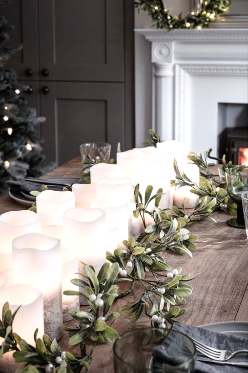a stylish Christmas table with a row of pillar candles, greenery and berries, grey plates and graphite grey napkins, grey glasses
