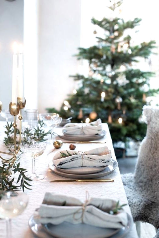 a stylish Christmas tablescape with grey plates, neutral linens, greenery, a tall brass candelabra with tall and thin candles