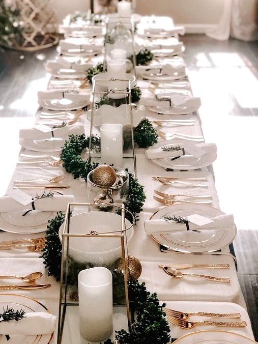 an elegant neutral Christmas tablescape with white linens, gold cutlery, gold and gold glitter ornaments, a greenery garland and pillar candles