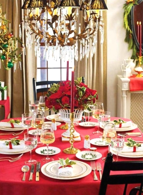 a chic Christmas tablescape with a red tablecloth, white porcelain, a lush red floral centerpiece and red candles, gold touches