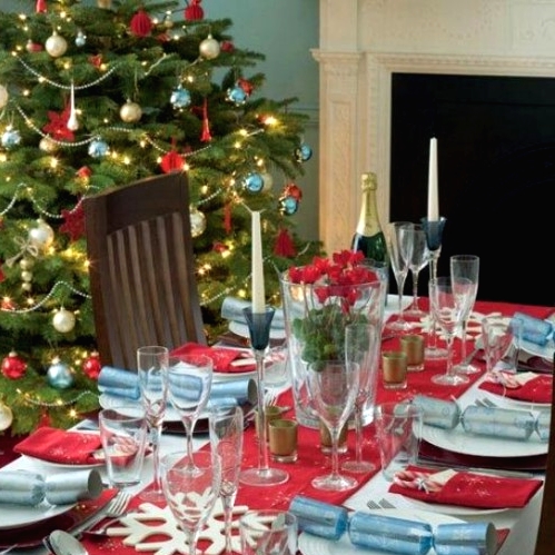 a bright Christmas tablescape with a red table runner, napkins, blue touches, snowflakes and red blooms