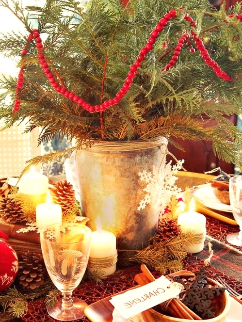 a rustic Chrismas tablescape with an evergreen arrangement with berries, pinecones and candles, a plaid tablecloth and a woven placemat