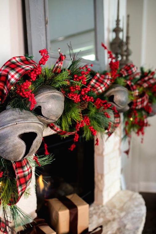a rustic Christmas mantel with an evergreen garland with berries, red plaid ribbon and oversized bruch Christmas bells