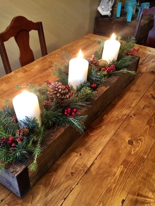 a wooden planter with evergreens, pinecones, berries and pillar candles is a lovely rustic Christmas centerpiece or decoration