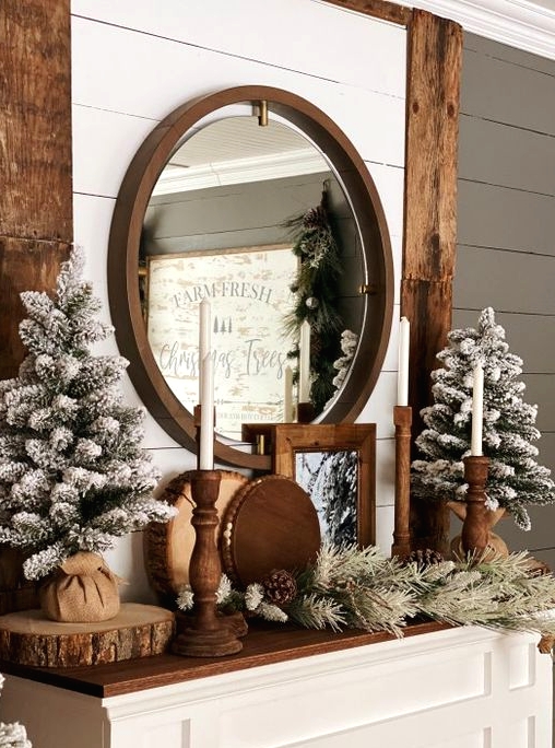lovely rustic Christmas mantel with evergreens, flocked Christmas trees, wooden candleholders, pinecones and wood slices