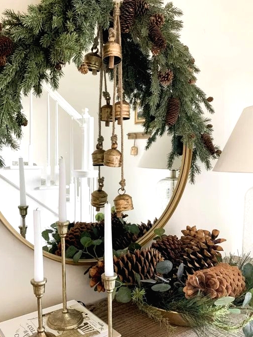 pretty Christmas decor with evergreens, pinecones, vintage brass bells, tall and thin candles is a lovely idea