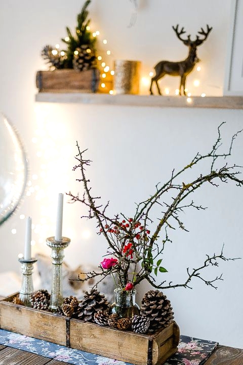 rustic Christmas decor with a wooden box with pinecones, candles, branches and berries, a crate with pinecones and a deer on the shelf
