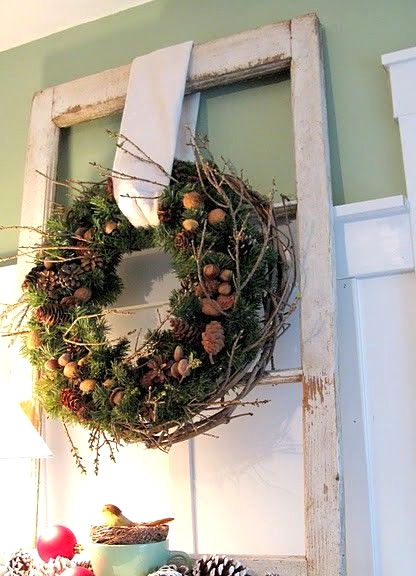 an evergreen Christmas wreath with pinecones, acorns, nuts, twigs, snowy pinecones and ornaments under it on the table for a cozy rustic holiday feel