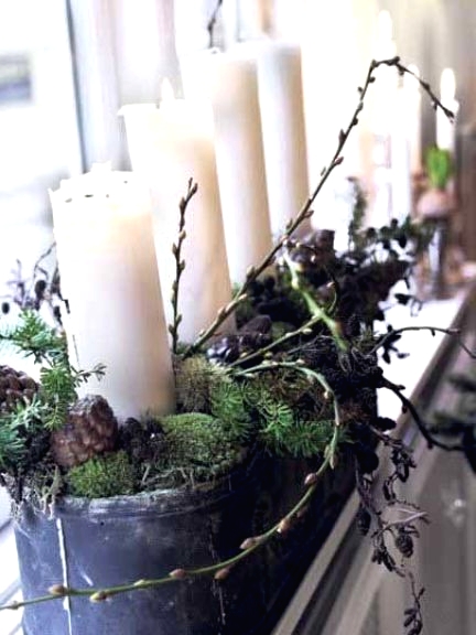 a metal planter with moss, branches, twigs, pinecones and pillar candles is an amazing way to bring a Nordic rustic feel to the space