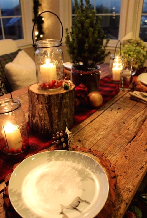 a rustic Christmas tablescape with a red burlap ribbon, candle lanterns, a mini tree and tree stump, wood slice placemats and pinecones all over
