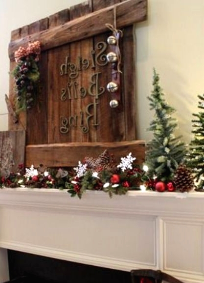 a lovely rustic Christmas mantel with a wooden sign with bells, an evergreen garland with pinecones, berries, ornaments and mini Christmas trees