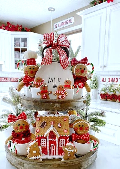 a wooden stand with snowy evergreens, mugs, plates, felt gingerbread ornaments, a real gingerbread house and a red plaid bow