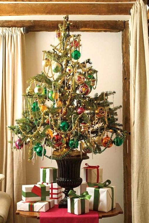 a bright vintage-inspired Christmas tree in an urn, decorated with pink, emerald and orange ornaments and beaded garlands