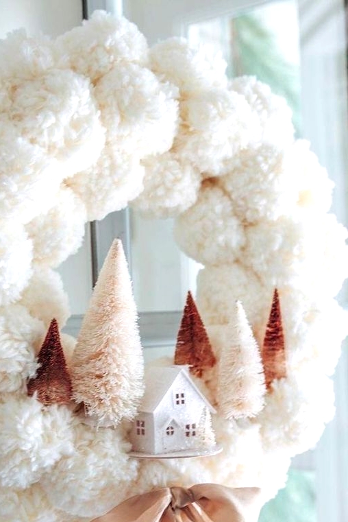 a delicate white pompom Christmas wreath with blush and rustic bottle brush trees and a mini house plus a mauve bow