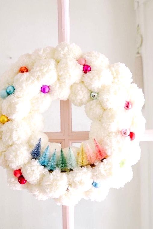 a white pompom Christmas wreat decorated with colorful ornaments and colorful bottle brush Christmas trees