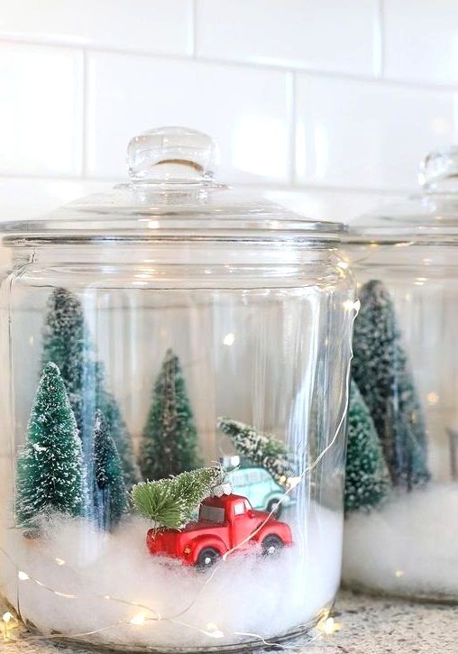 a Christmas terrarium made of a large jar with faux snow, bottle brush trees and a large truck plus lights around