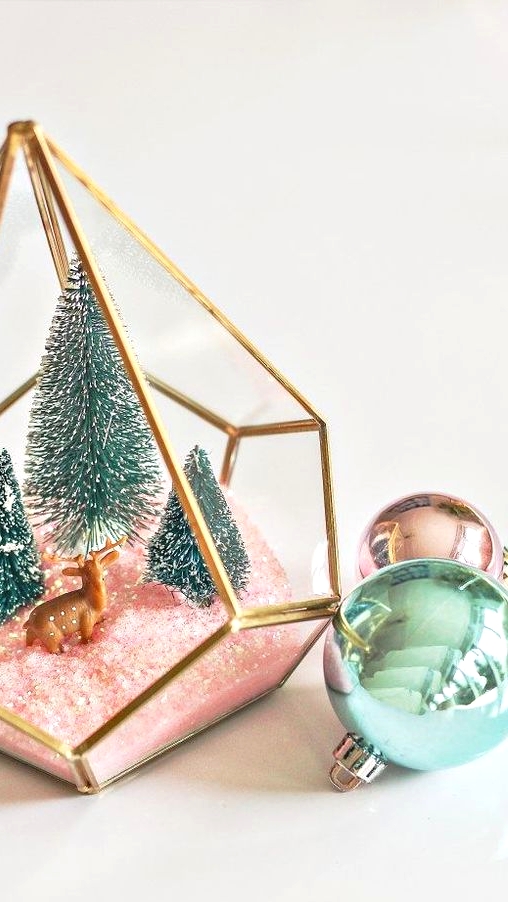 an elegant Christmas terrarium with pink faux snow, green bottle brush trees and a little deer figurine is chic and cute