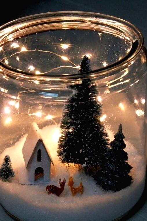 an oversized jar with faux snow, little deer figurines, a house and some bottle brush trees and lights is pure magic