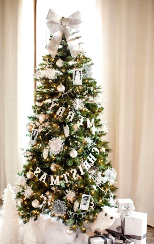 a sophisticated Christmas tree with lights, with white and gold ornaments, photos, buntings and paper pompoms plus a silver bow on top