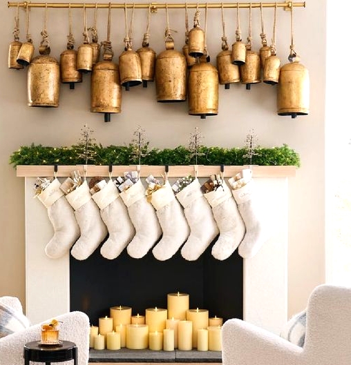 lovely Christmas decor with oversized gold and brass bells, white stockings, an evergreen garland with lights and pillar candles