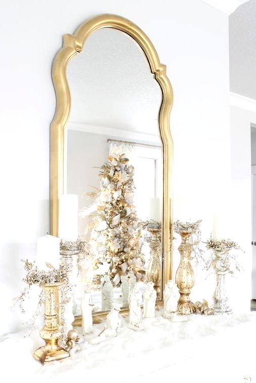 an elegant gold and white Christmas mantel covered with faux fur, with gold candleholders, candles and a mirror in a gold frame