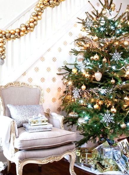 a gold ornament garland on the railing, a Christmas tree with silver and gold ornaments, lights and white snowflakes
