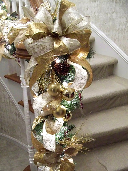 refined gold and white Christmas railing decor with gold and white embroidered ribbons and a bow, ornaments, pinecones and lights