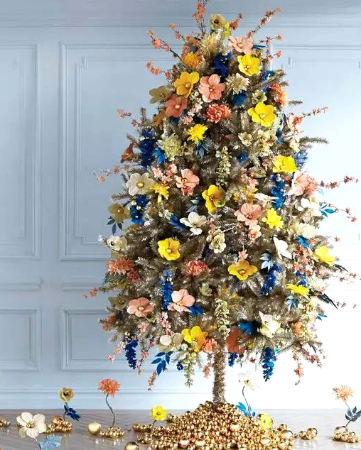 a unique gold Christmas tree decorated with yellow, blush, electric blue faux flowers and blooming branches and with bells on the base