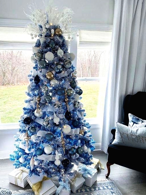 a blue Christmas tree with white, blue, navy, gold and silver ornaments, branches with pompoms and white ribbons for a beach or coastal space