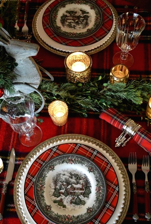 a bold traditional Christmas tablescape with a plaid tablecloth, chargers and napkins, greenery garlands, candles and chic burgundy cutlery