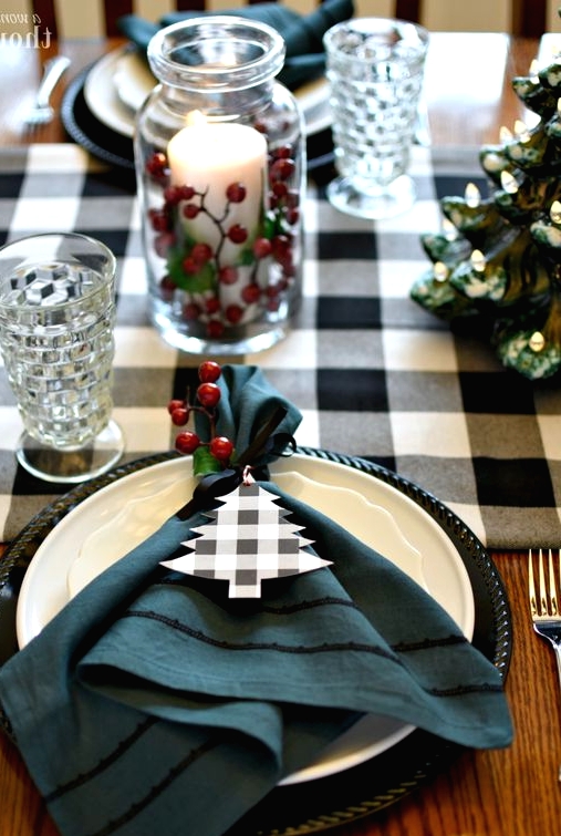 a lovely Christmas tablescape with a buffalo check runner and napkin tags, berries and a pillar candle in a jar and elegant glasses