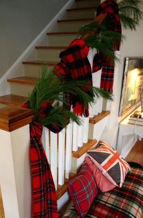 pretty Christmas decor with evergreens and plaid scarves on the railing, a plaid bench with plaid pillows is very cozy