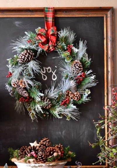 a flocked evergreen wreath with pinecones, berries, a red plaid bow is a pretty and cool decoration for indoor and outdoor decor